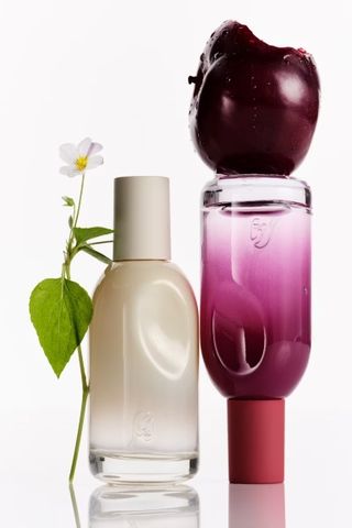 two glossier perfume bottles on white background with a flower and apple