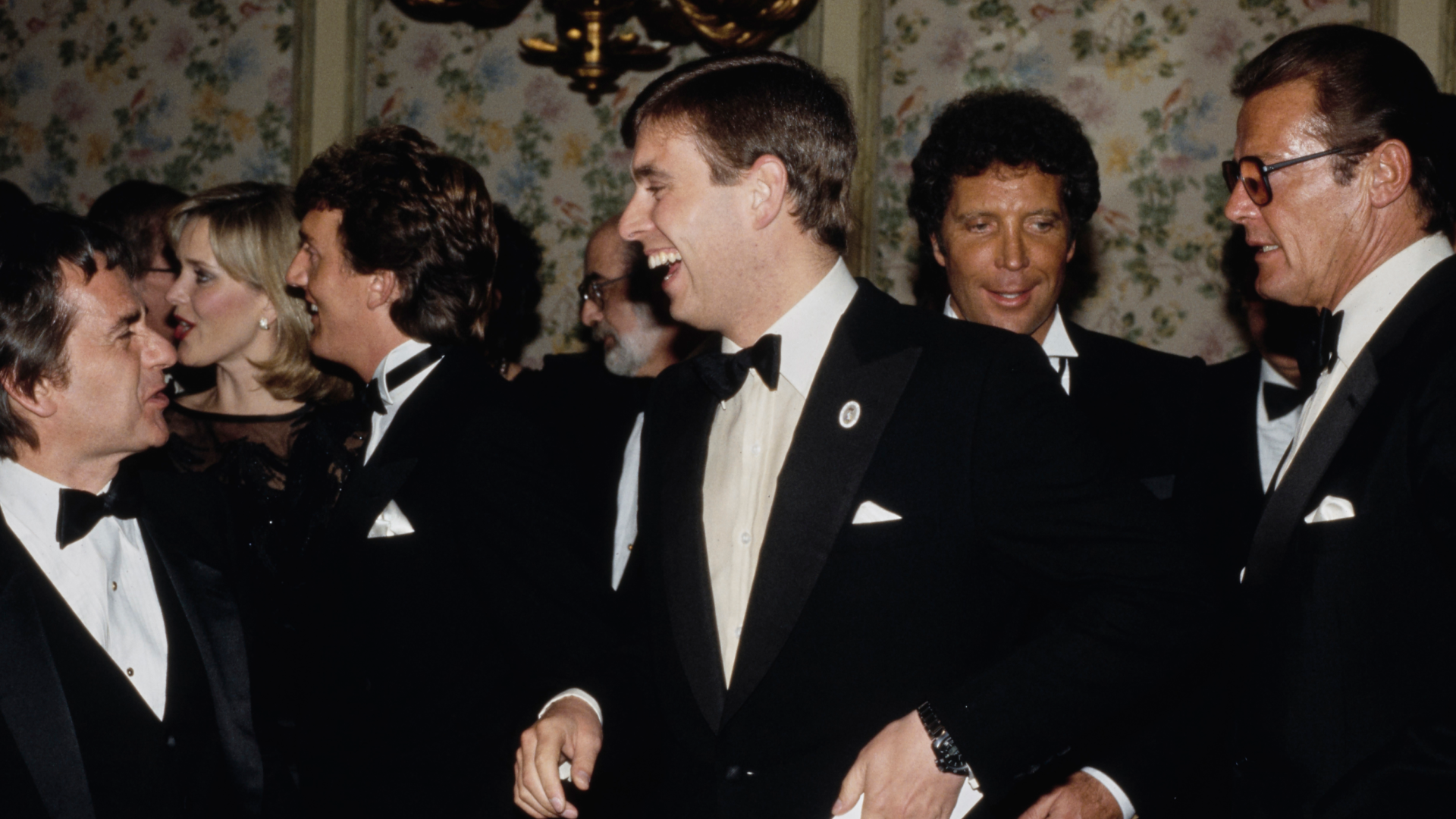 Prince Andrew in a tuxedo, laughing with Tom Jones standing behind him 