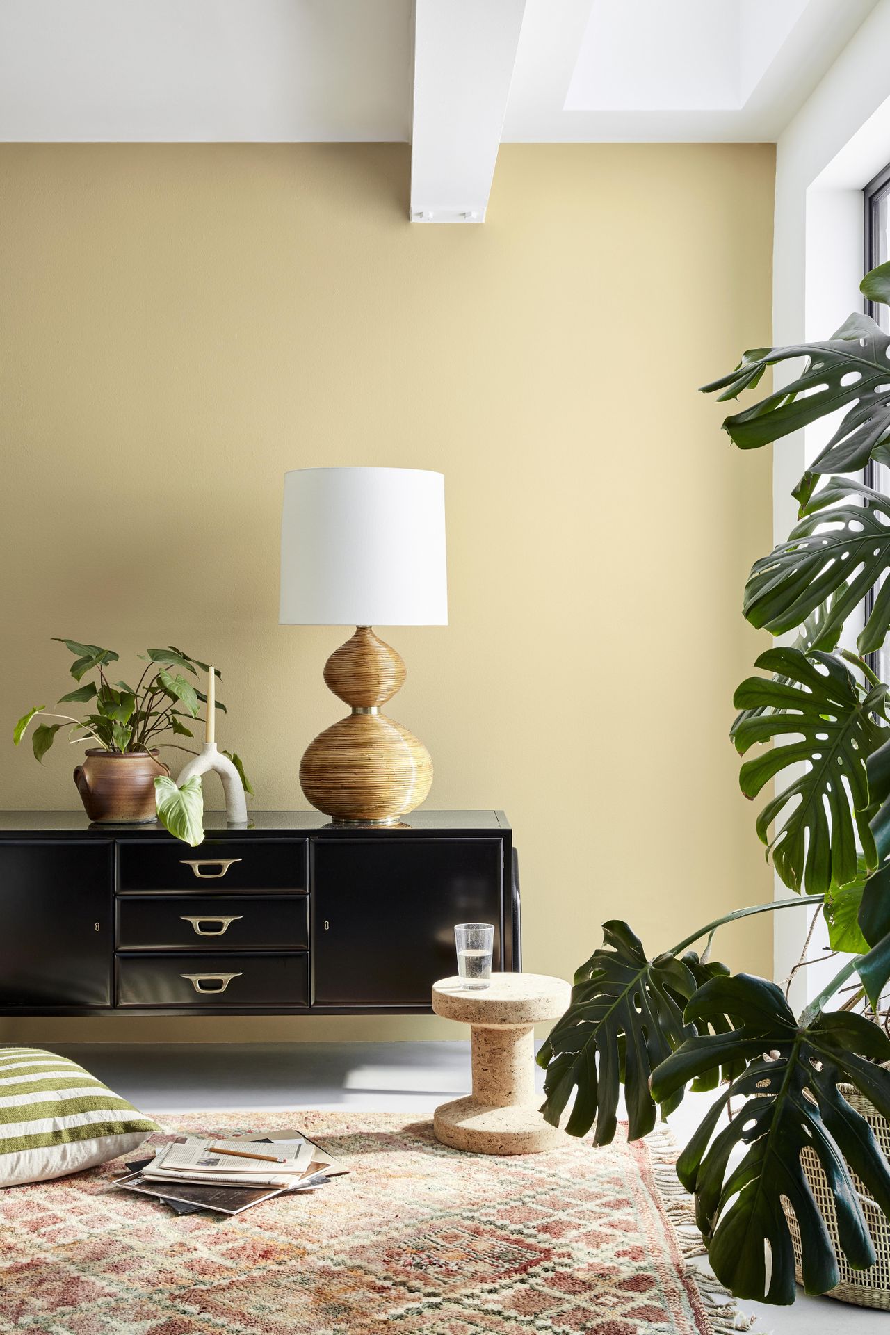 living room with beige elements, black sideboard, ecru walls, white woodwork, plants, patterned rug, cork stool, cushion on floor