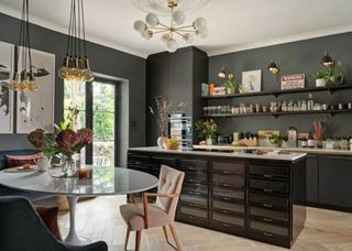 haberdashery style kitchen island with black kitchen cabinets. On the left is a white dining table with blue and pink chairs.