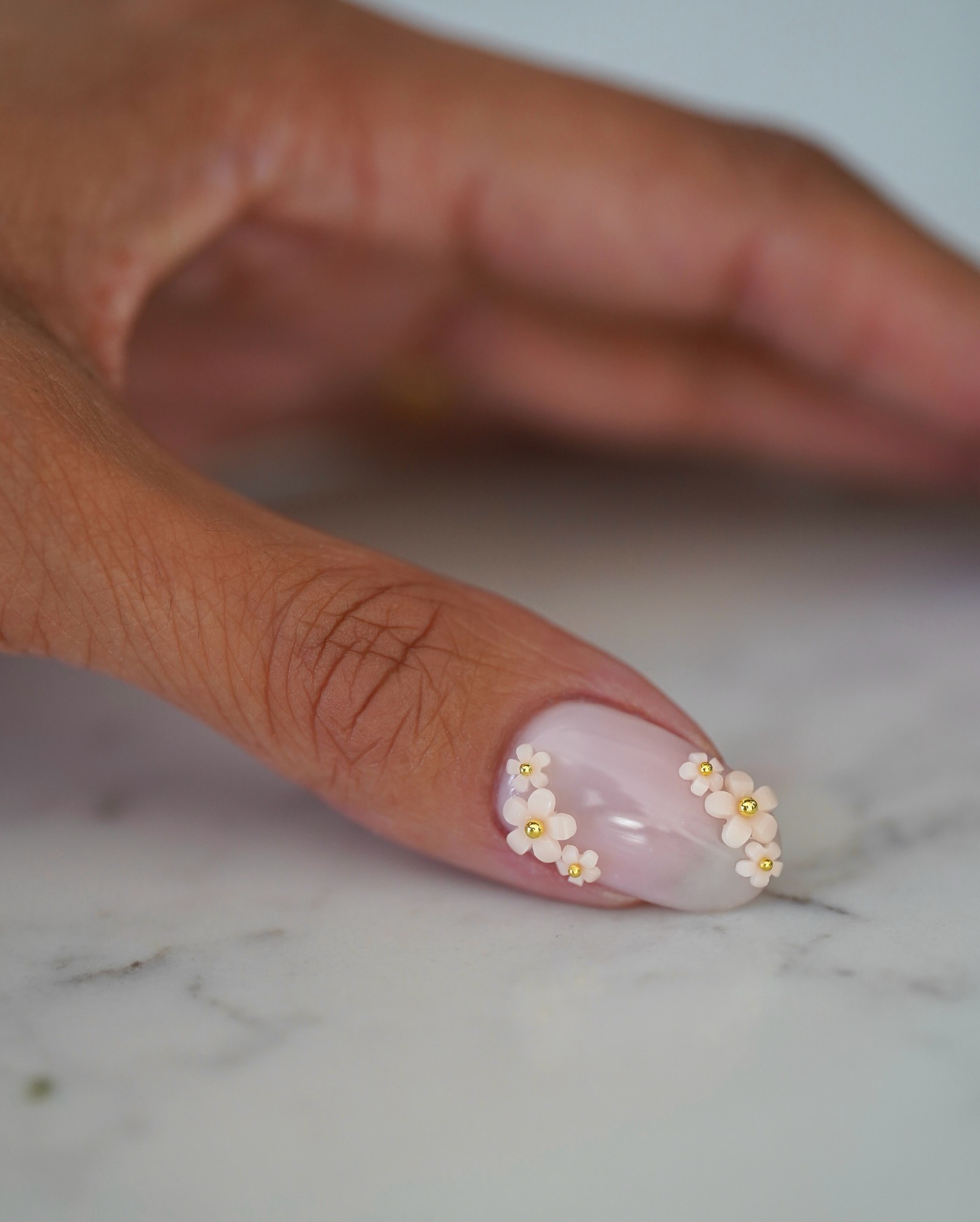 A close-up of a sheer, milky manicure with delicate 3D floral nail art