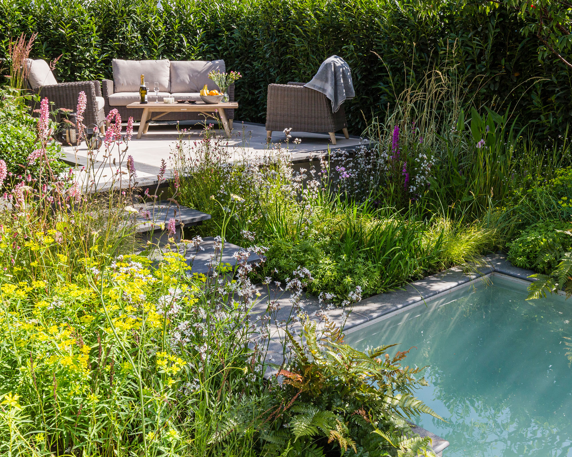 raised patio area with garden furniture and steps leading up to it, with planted areas and a natural pool feature
