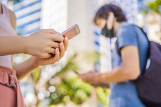 People with masks walking while looking at their phones.