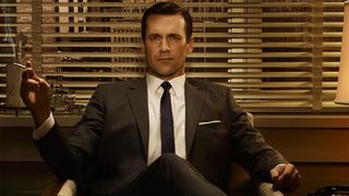 Jon Hamm as Don Draper in Mad Men, smoking a cigarette in a chair.