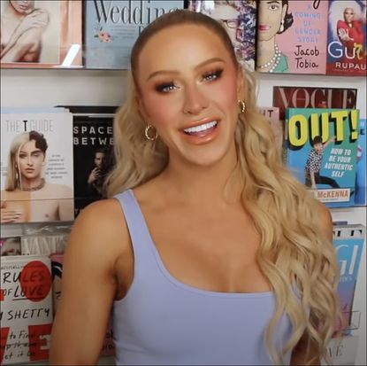 Gigi Gorgeous standing in front of wall of books 