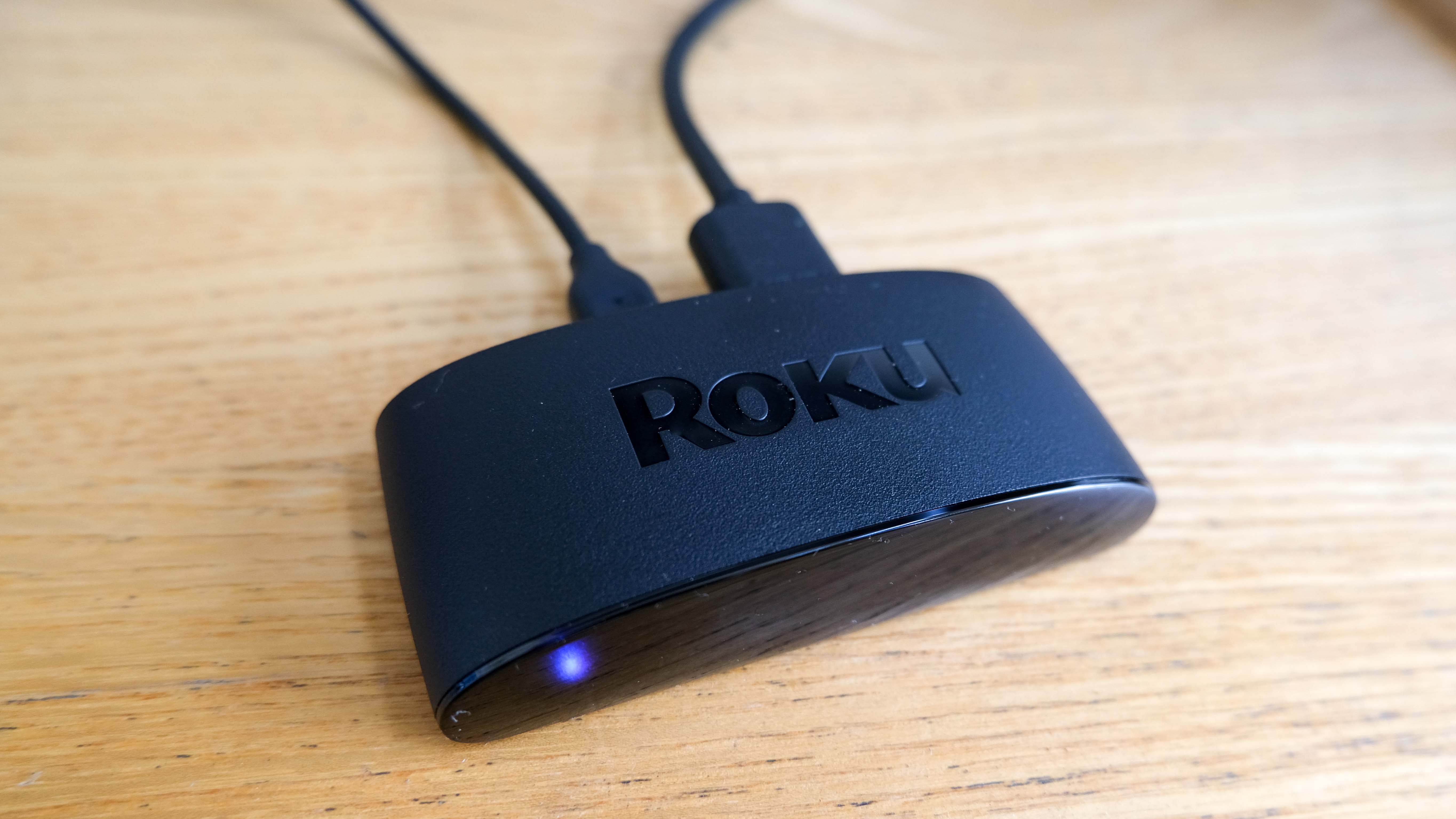 The Roku Express 4K Plus, turned on and plugged in, on a wooden surface, is one of the Best Roku Devices.