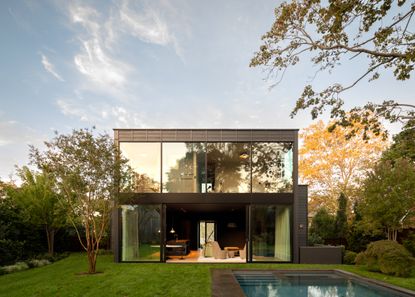 rectangular sag harbour house with glazed facade and open curtains looking towards garden and swimming pool