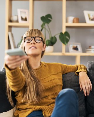 A woman reaching her arm out holding a TV remote