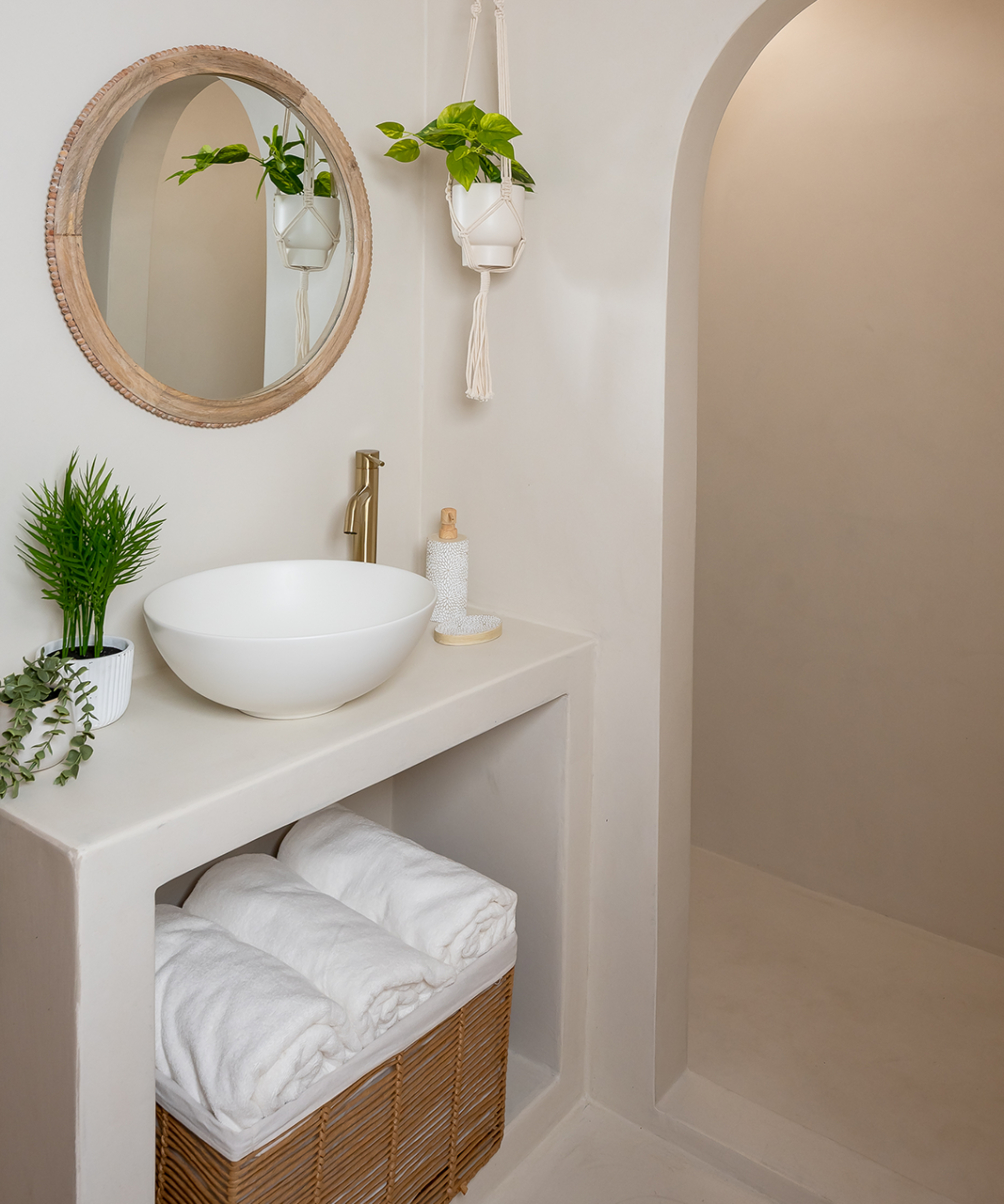 microcement bathroom in off white stucco finish with built in vanity unit, white countertop sink and arch leading to walk in shower