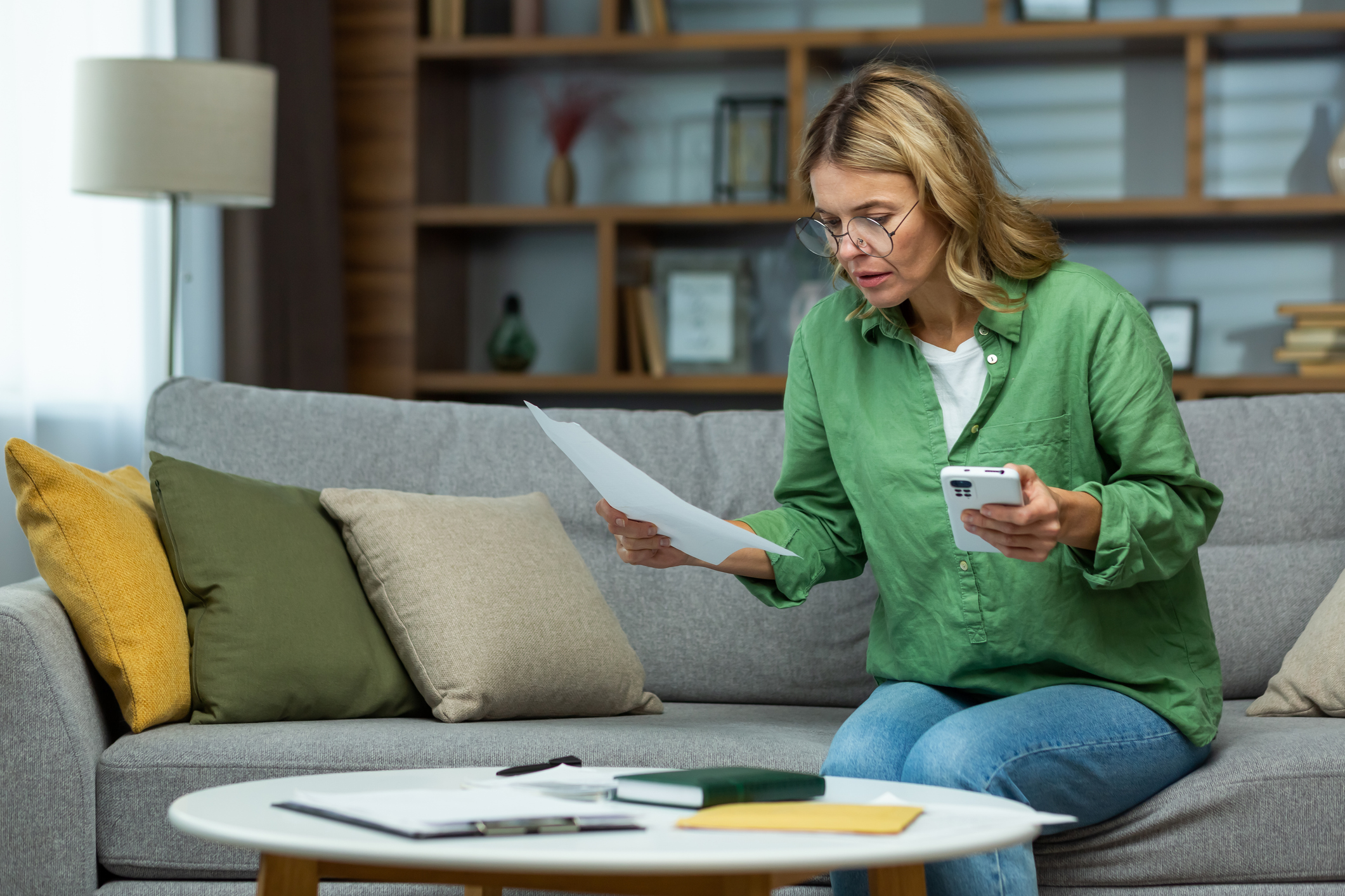 Woman at home on sofa with phone checking tax bills 