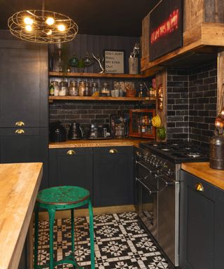 A black kitchen with black ceiling, black and white tiled kitchen flooring, black metro tiles and shelving
