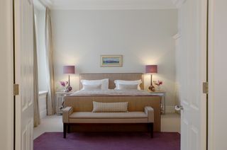 bedroom with TV in end of bed, matching table lamps, pink and cream scheme, drapes, bench at foot of bed