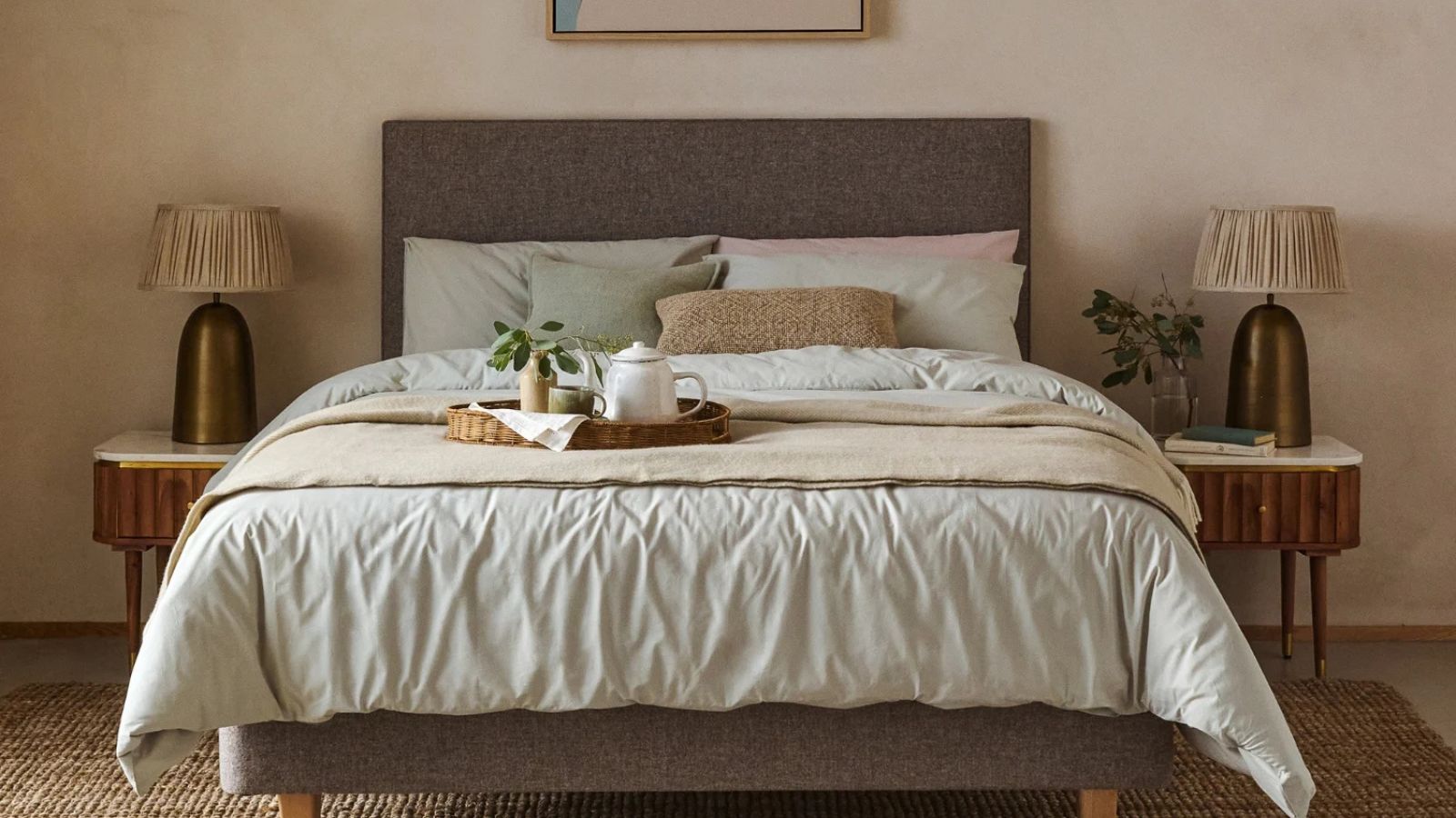 Beige bedding on a gray bed frame against a cream wall; a nightstand either side of the bed.