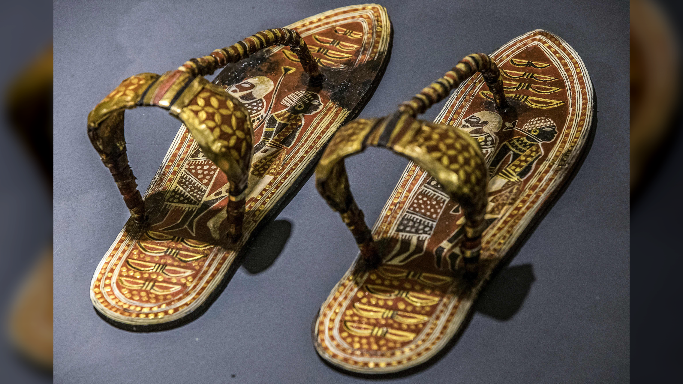 a pair of decorated wood-and-leather sandals on a grayish table