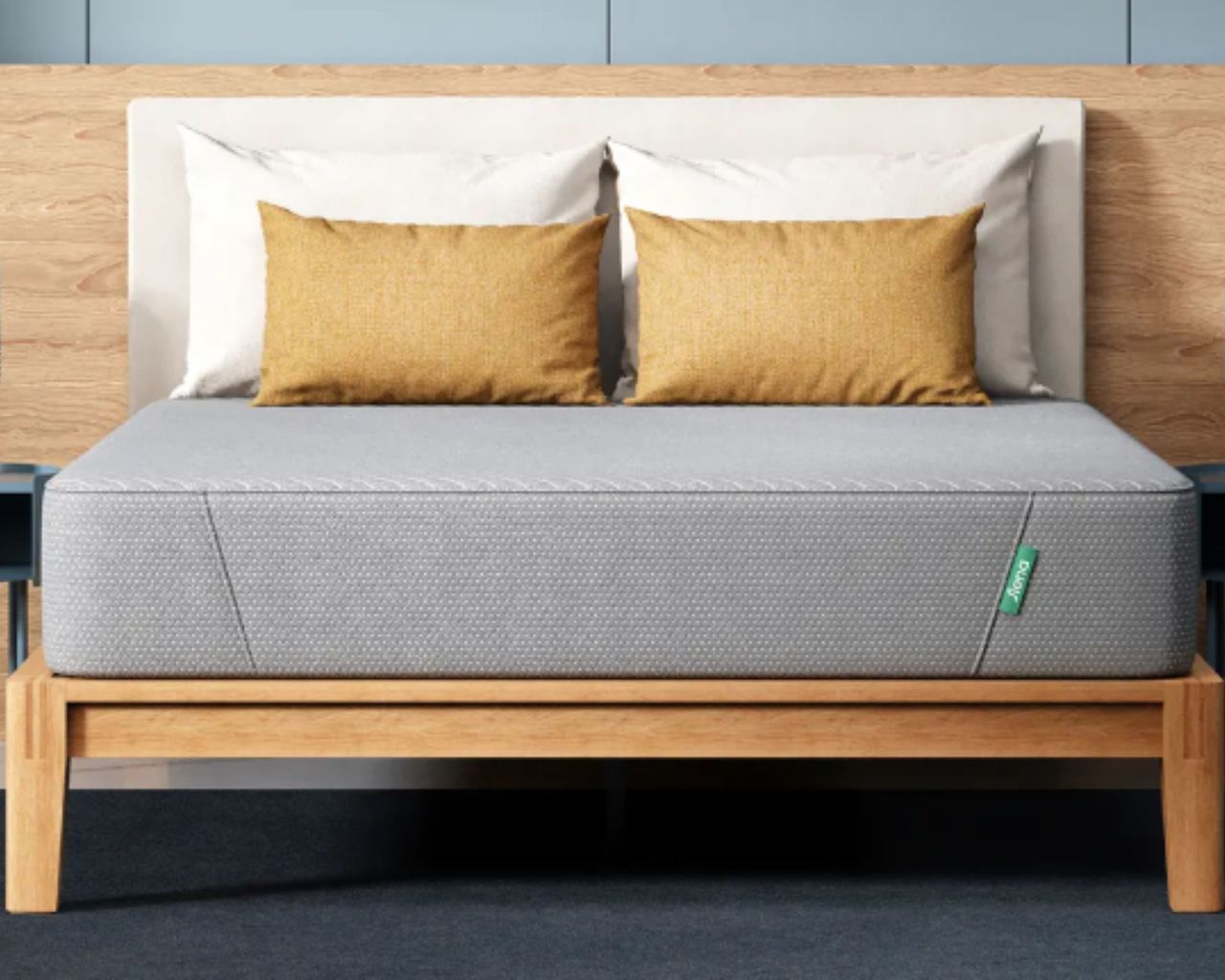 Grey Siena memory foam mattress with white and yellow cushions and pillows on a wooden bedframe with white headboard, and wood and blue panelled wall behind.