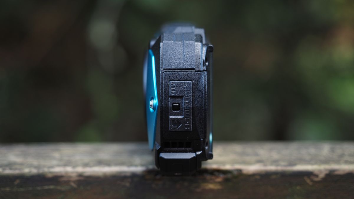 Close up of a Pentax WG-90 sitting on a wooden surface in front of woodland