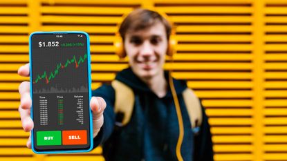 Young man with backpack and headphones holding up smartphone to show stocks he may buy or sell