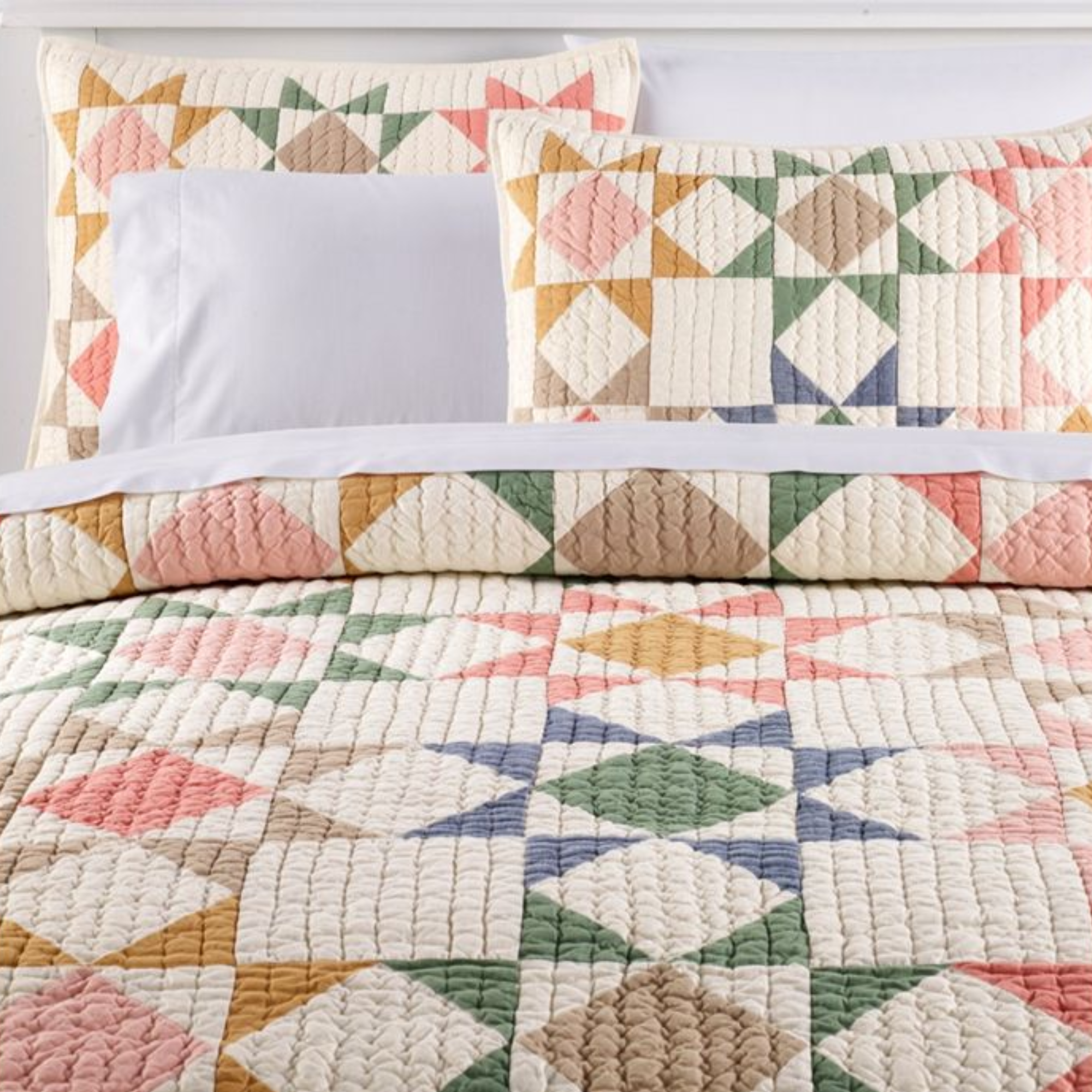 a patchwork quilt and two pillows in shades of green, white, orange, red, and pink