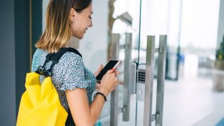 Rear view of woman in casual wear checking code for entering building on mobile phone