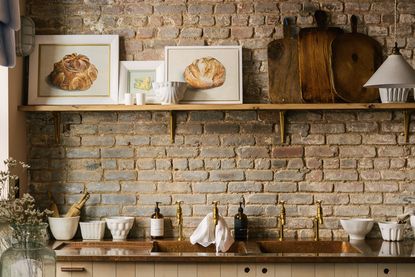 Rustic kitchen ideas - an exposed brick wall lined with chopping boards and cookware