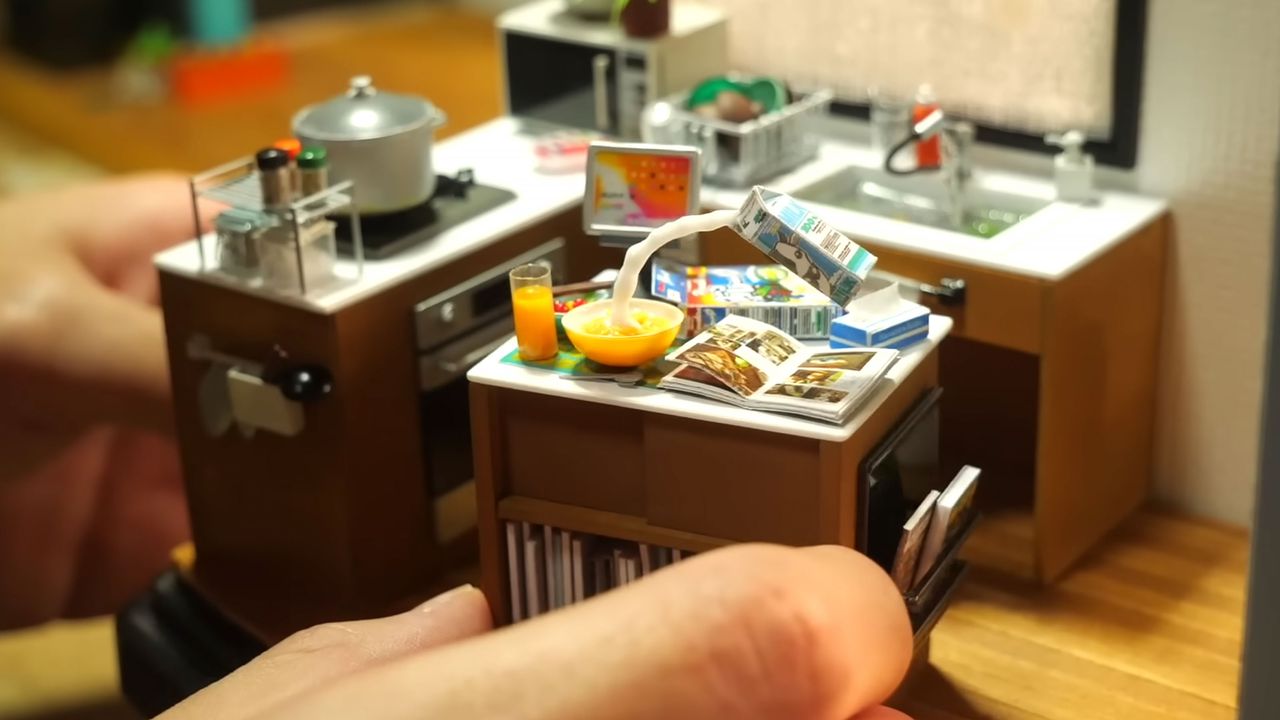 A shot of a miniature kitchen diorama with a hand in shot.