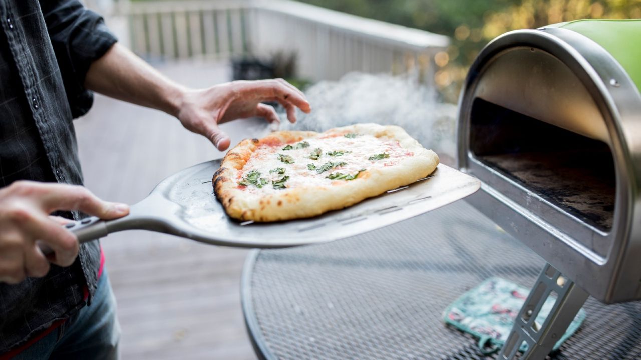 Midsection of man examining food on pizza peel by oven at porch - stock photo