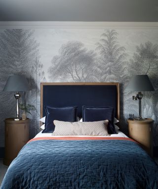 blue bedroom with gray tree wall mural, bed with dark blue headboard and navy cushions