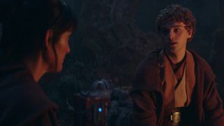 An older female Jedi is talking to a younger male Jedi whilst they are sitting at a glowing fire.
