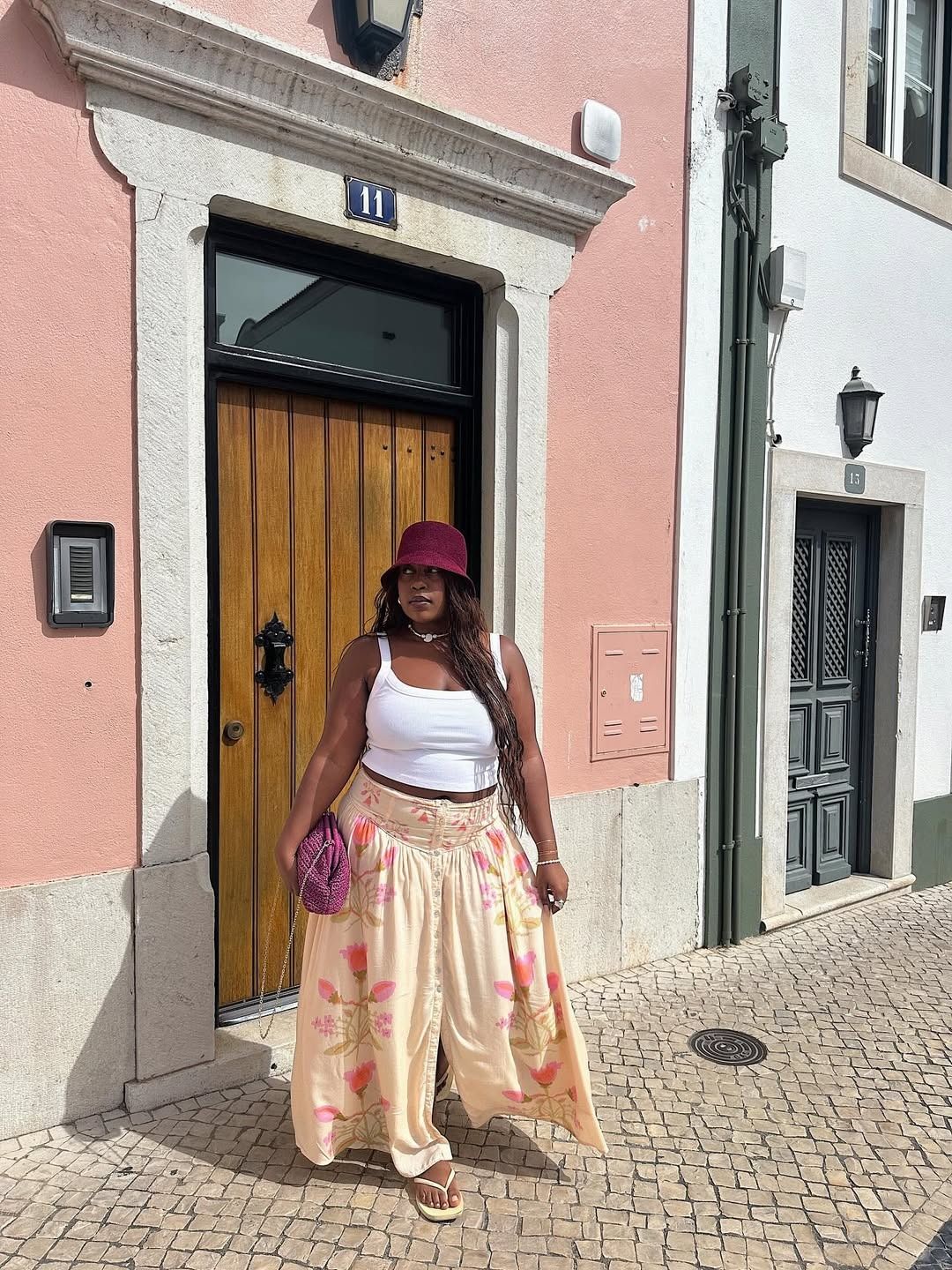 Aniyah wears a white tank top, floral skirt, and pink raffia bag.
