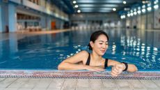 Woman looking at watch, leaning on the edge of the pool smiling