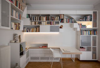 Acropolis 13 by Natalia Bazaiou focusses on white shelving installation with books on a side board and small desk and chair.