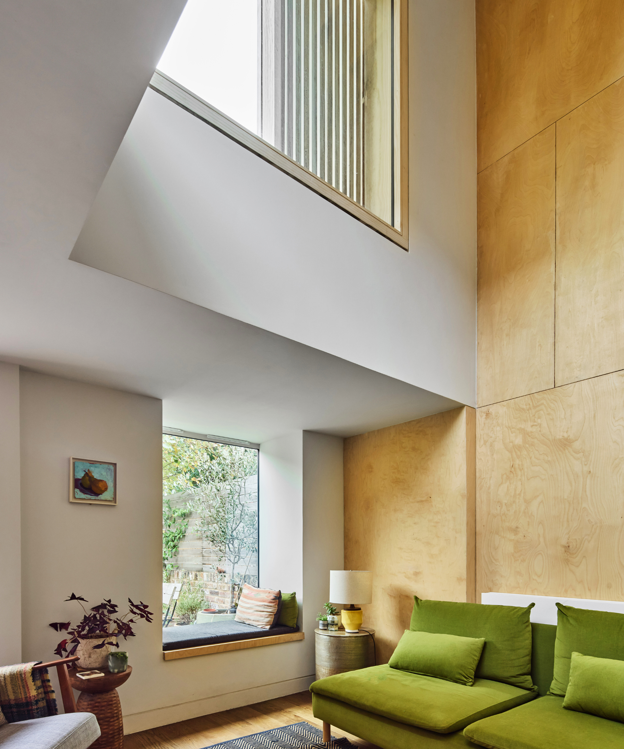 Living area with green sofa, window seat, and a large window at the top of the wall with blinds