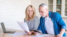 Worried mature man and woman check finance account in kitchen