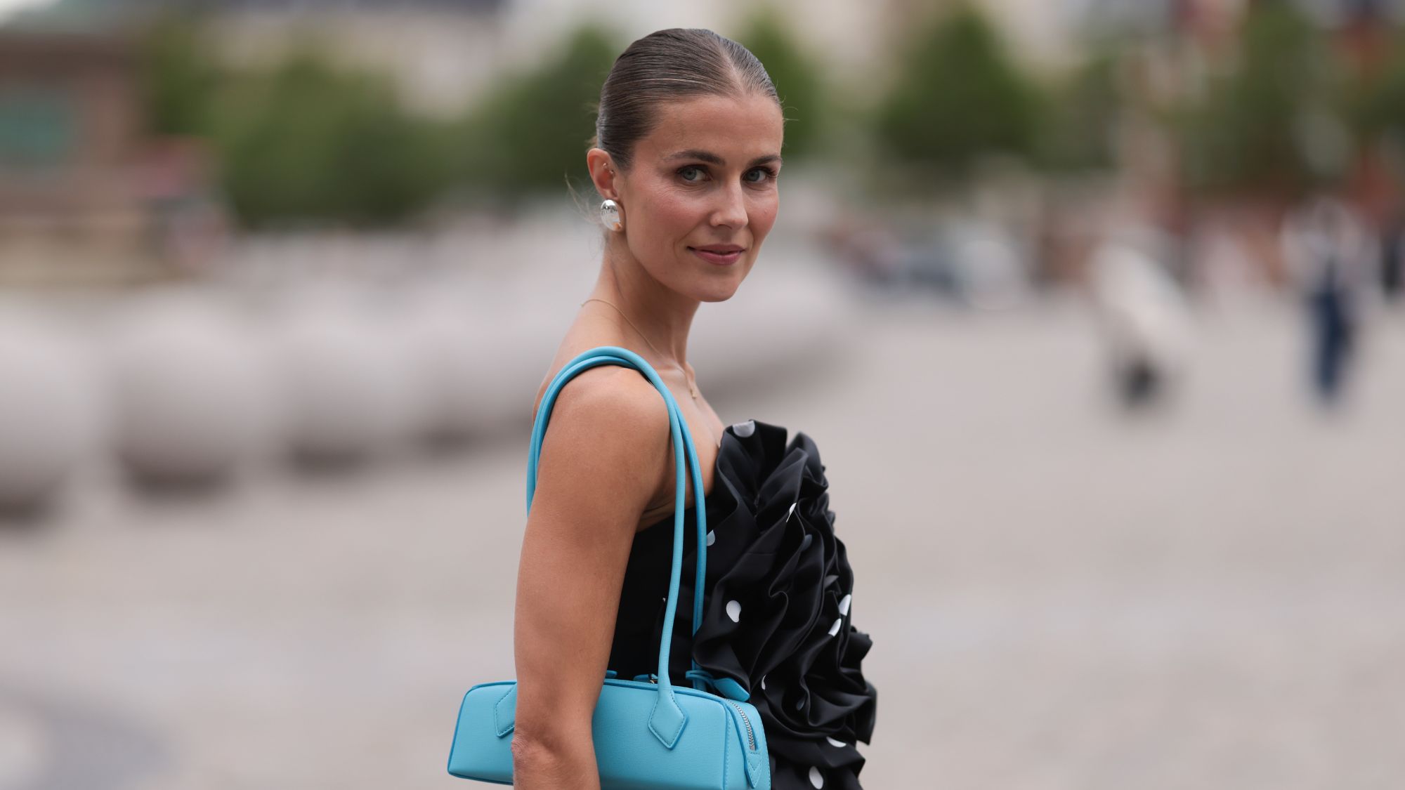 best bronzers for pale skin - woman with bronzed cheeks, slicked back hair and a blue handbag