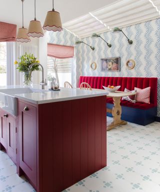 Deep red island, blue and white wallpaper, bench seating area, green and white floor tiles, pendant lights