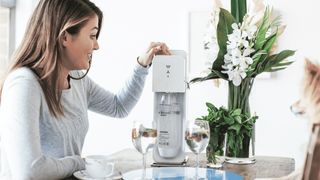 En ung kvinde betjener en SodaStream maskine ved køkkenbordet