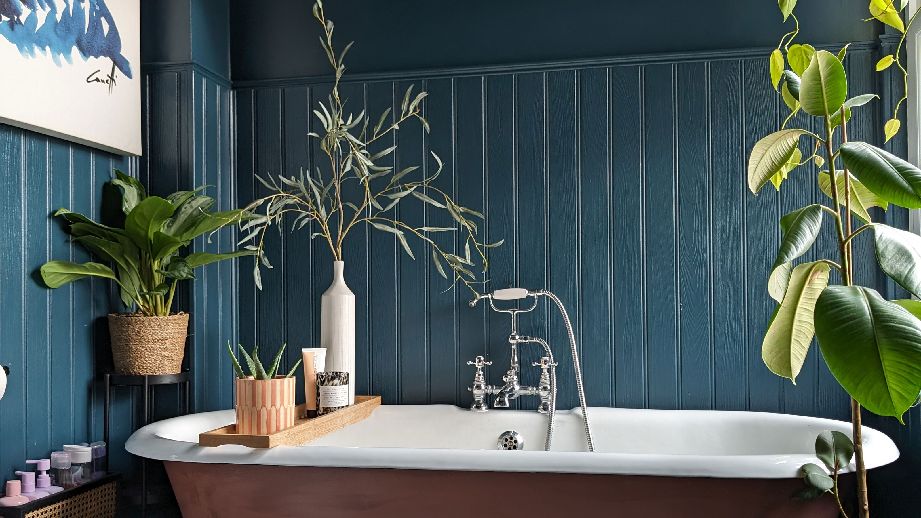 Bathroom with teal wall panelling and painted roll top bath surrounded by houseplants