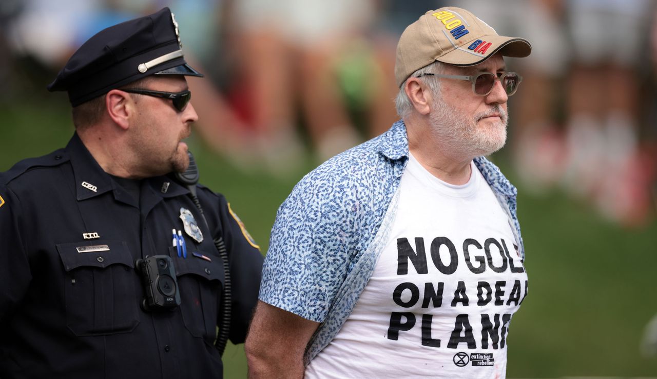 A protestor is taken away from the 18th green in handcuffs