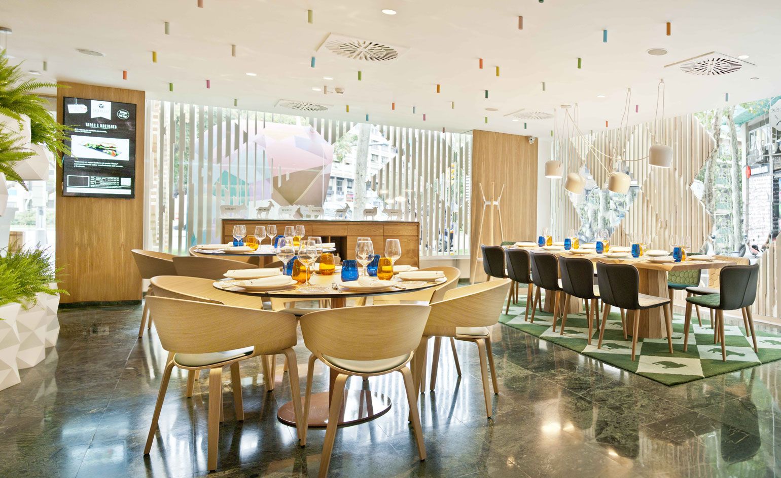 A restaurant with decorated tables, chairs, potted plants, dark marble flooring, a decorated ceiling and large windows.