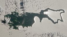 An astronaut photo of an island with sunlight reflecting off a lake making the landmass look like a magnifying glass