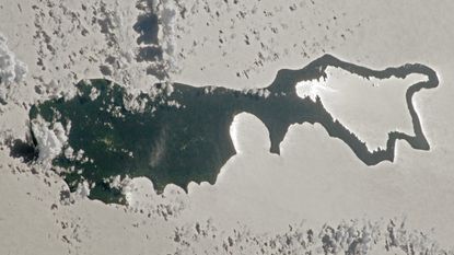 An astronaut photo of an island with sunlight reflecting off a lake making the landmass look like a magnifying glass