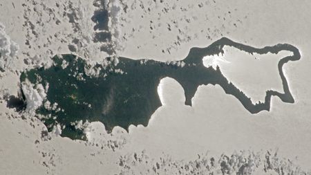 An astronaut photo of an island with sunlight reflecting off a lake making the landmass look like a magnifying glass