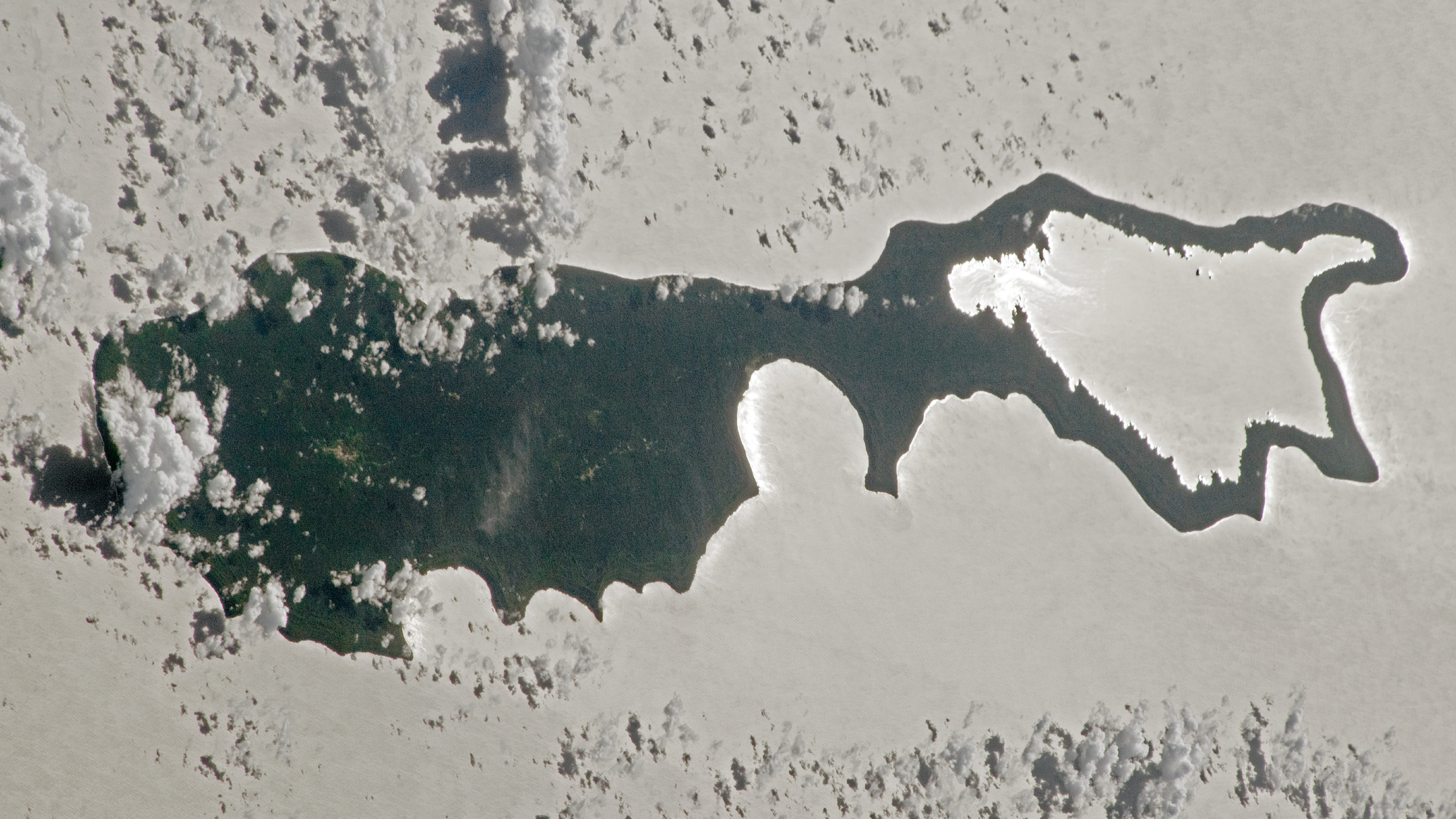 An astronaut photo of an island with sunlight reflecting off a lake making the landmass look like a magnifying glass