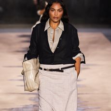 A model on the Hugo Boss runway wearing a black cardigan and white belted skirt