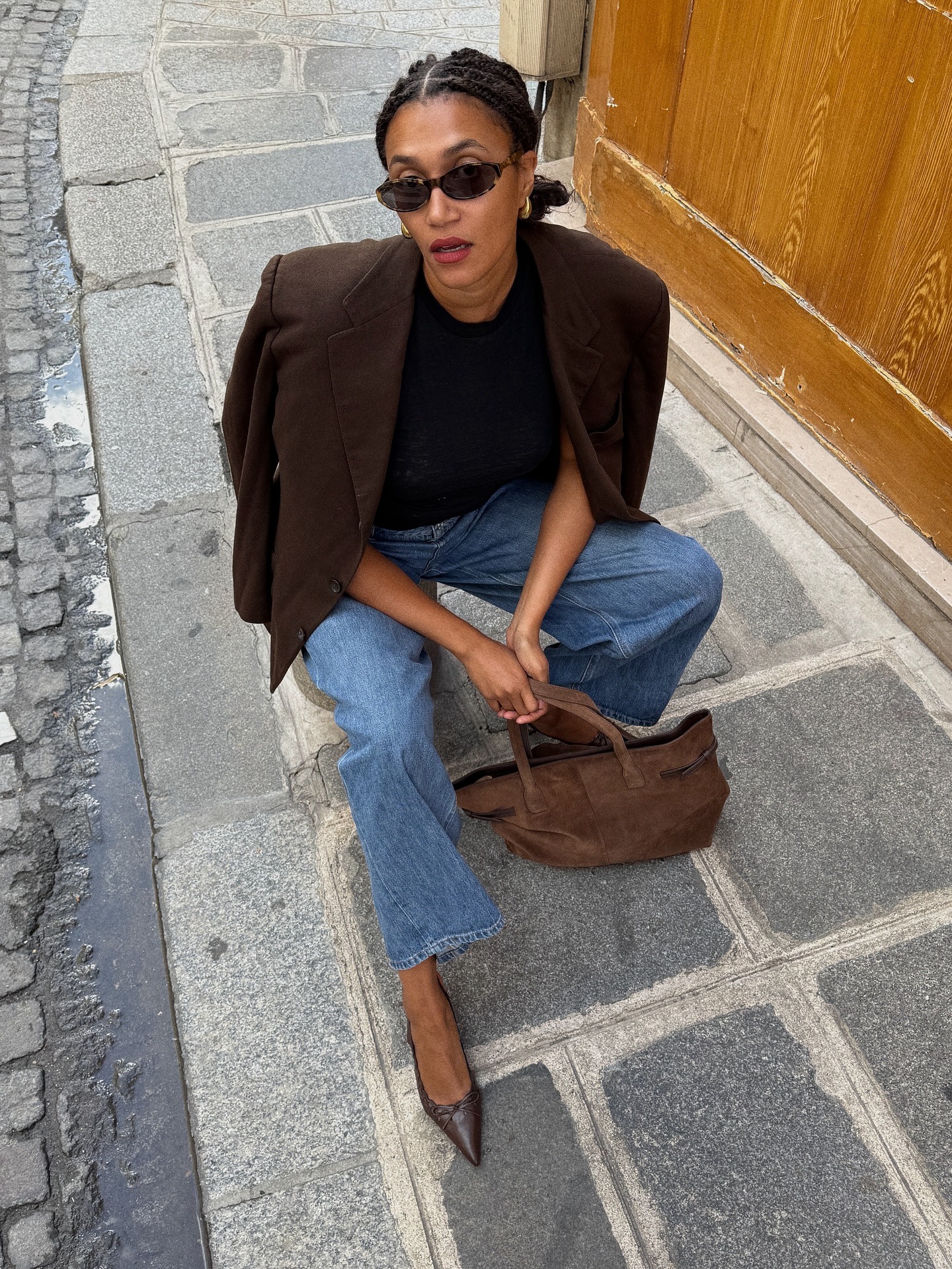 @lenafarl wearing a brown blazer, jeans, and a brown suede bag.