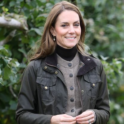 Princess Kate wearing a jacket and sweater standing in front of trees
