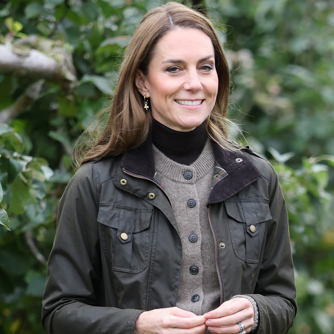 Princess Kate wearing a jacket and sweater standing in front of trees