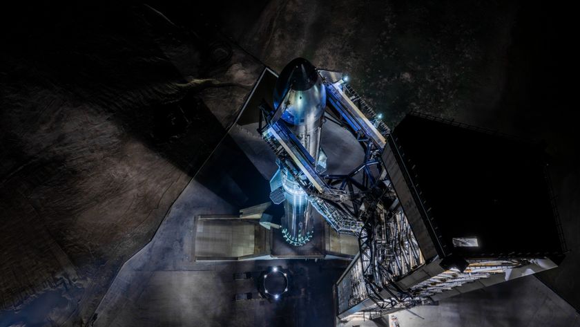 A giant steel rocket stands next to a launch tower lit by spotlights in the dark of night.