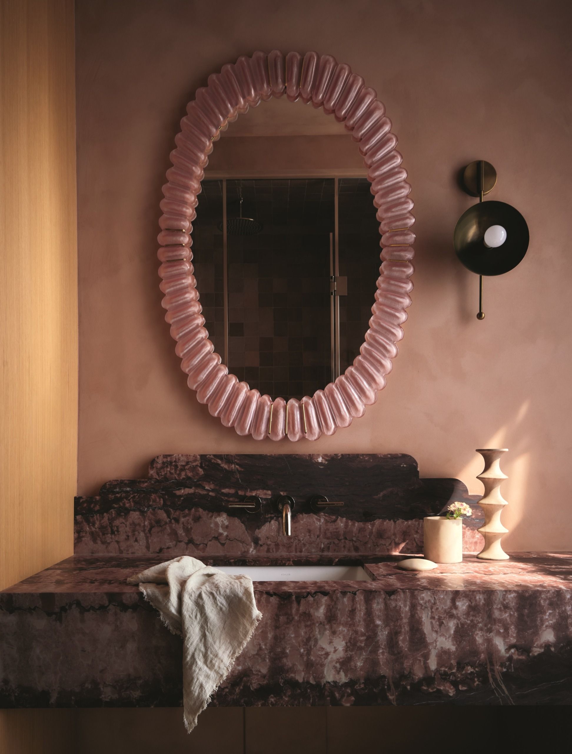 a neutral coloured bathroom with a pink glass mirror and a textured stone sink
