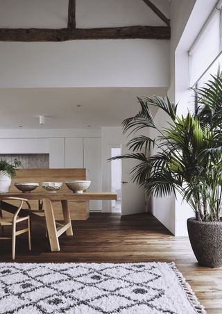 open plan living space with boho style rug, wood table and chairs, island, hardwood floor, paint, white walls, beams